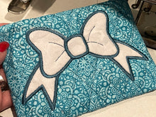 Teal fabric with a white bow design held by a hand.
