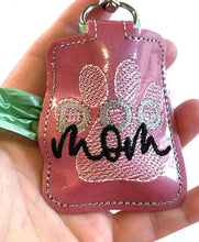Dog Mom doggy waste bag holder in the hoop machine embroidery design file from Designs by Babymoon Photo shows size in adult hand with hardware clip at the top and opening in the side for waste bags to be accessed for ease of use.